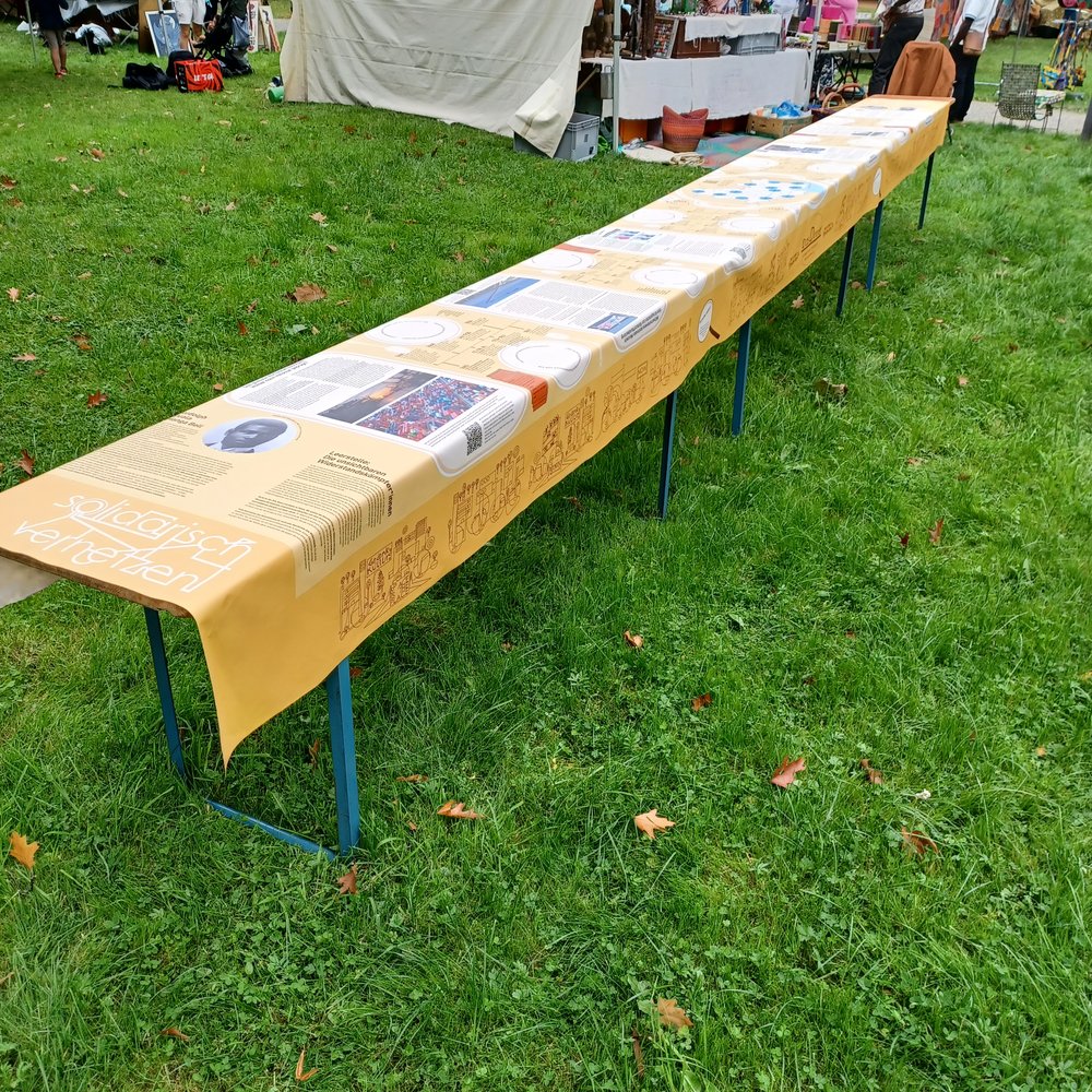 Die Ausstellung das Dinner als 6m langes Tischtuch bei einer öffentlichen Veranstaltung auf einer grünen Wiese