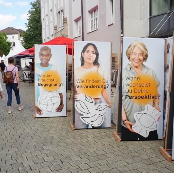 Banner der Ausstellung Niedersachsen weltbewegt stehen in einer Fußgängerzone. Auf Ihnen steht: Warum brauchst du Begegnung? Wie findest du Veränderung?