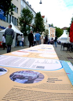 Eine Ausstellung über den Kolonialismus in Form einer Tischdecke. Im Fokus ist ein Beitrag über Anton Wilhelm Amo