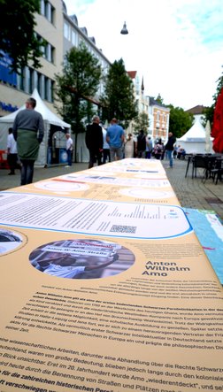 Eine Ausstellung über den Kolonialismus in Form einer Tischdecke. Im Fokus ist ein Beitrag über Anton Wilhelm Amo