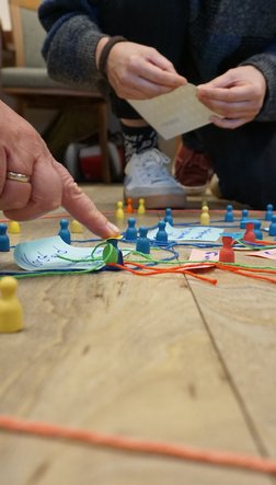 Ein Finger zeigt auf mehrere Spielfiguren, die auf dem Boden stehen