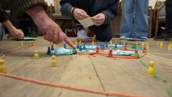 Ein Finger zeigt auf mehrere Spielfiguren, die auf dem Boden stehen