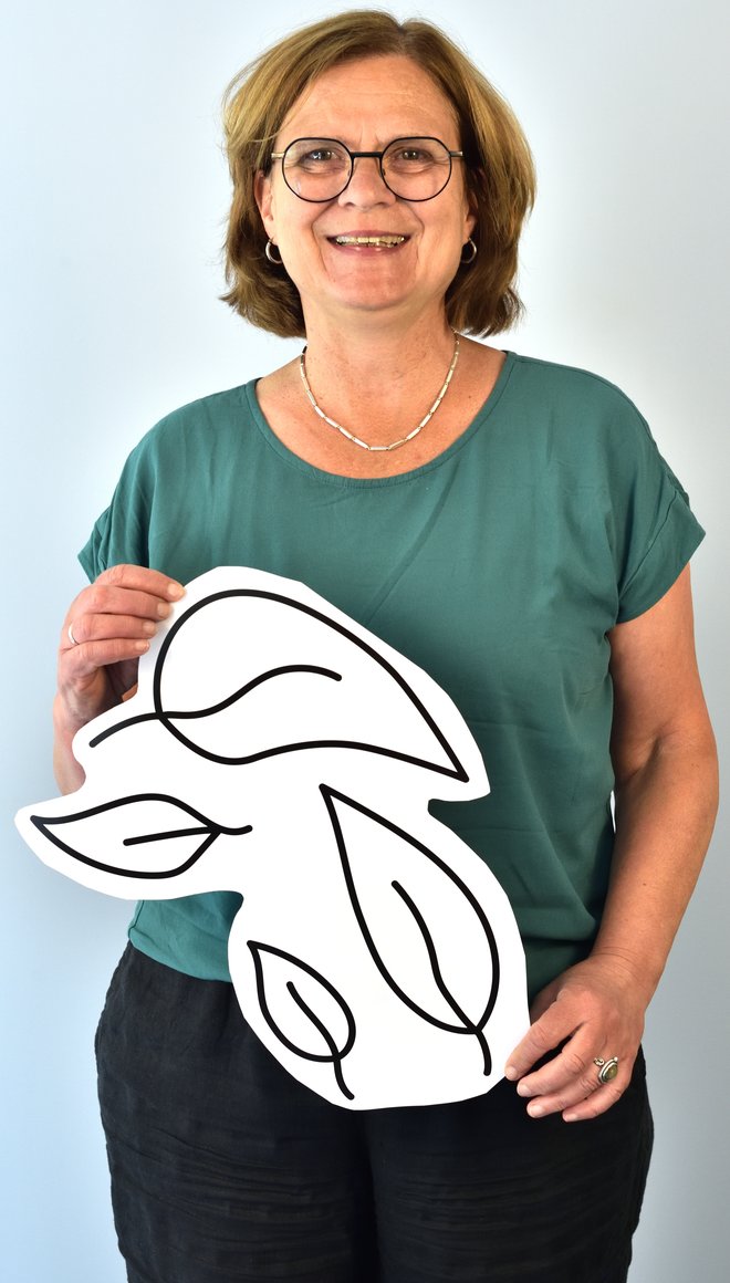 Portait von Gabi Janecki, die mittellange blonde Haare und weiße Haut hat und einen blaues Oberteil trägt