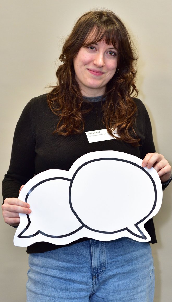 Dania hält lächelnd eine Zeichnung von zwei Sprechblasen in die Kamera.