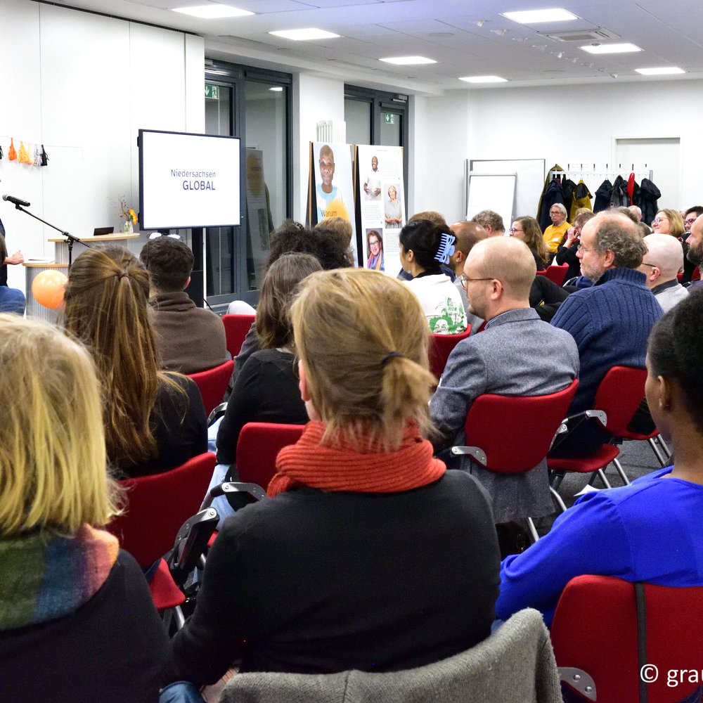 Viele Menschen sitzen in Reihen vor einem Stehpult