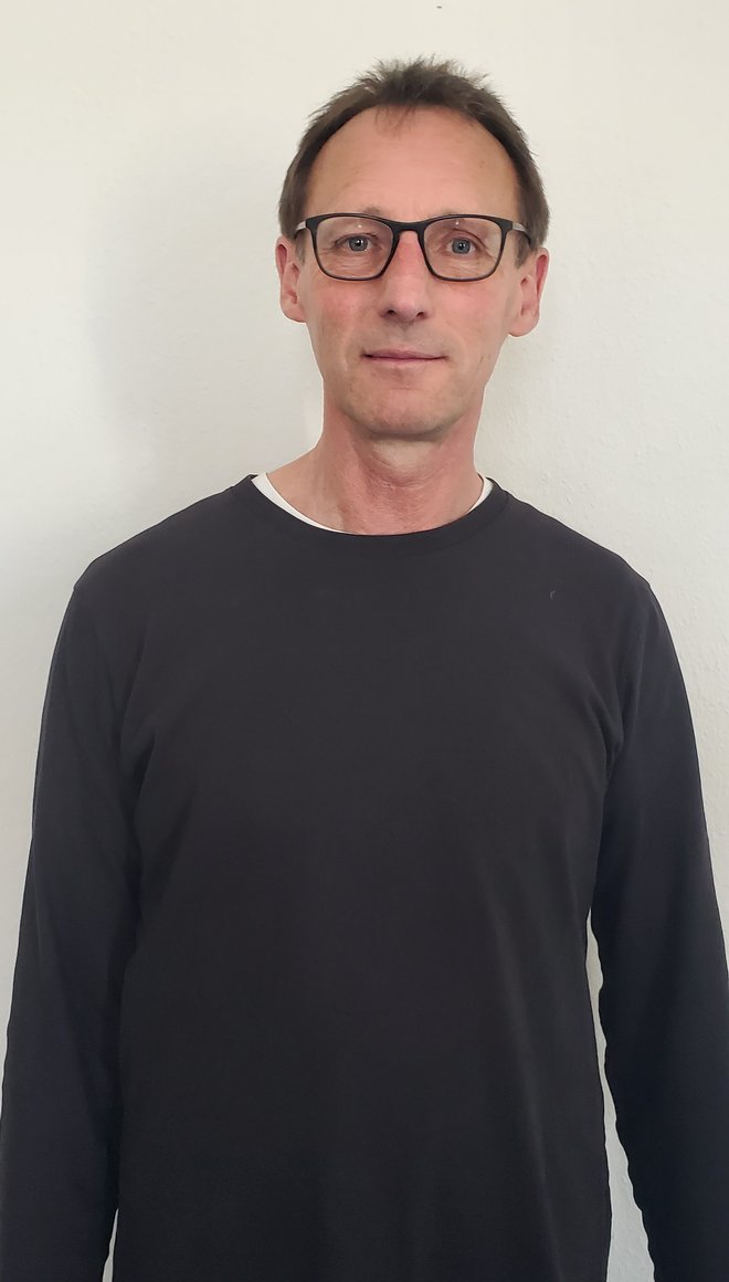 Dirk lächelt in die Kamera. Er trägt eine Bille und einen schwarzen Pullover.