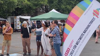 Menschen stehen vor einer Mitmachaktion draußen und tauschen sich aus