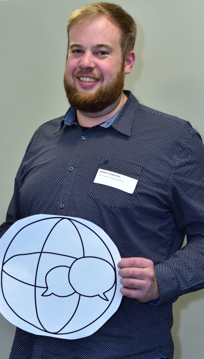 Malte hält lächelnd das Niedersachsen.GLOBAL Symbol für eine Globale Bewegung in die Kamera.