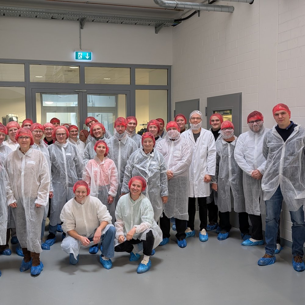 Teilnehmende stehen in Hygieneanzügen vor der Produktion