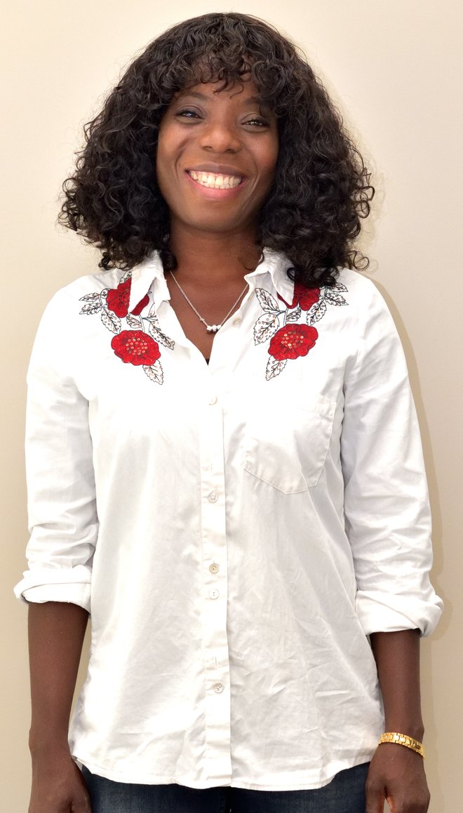 Portait von Mana Atiglo, die schwarze, mittellange Haare und schwarze Haut hat und ein weiße Bluse trägt