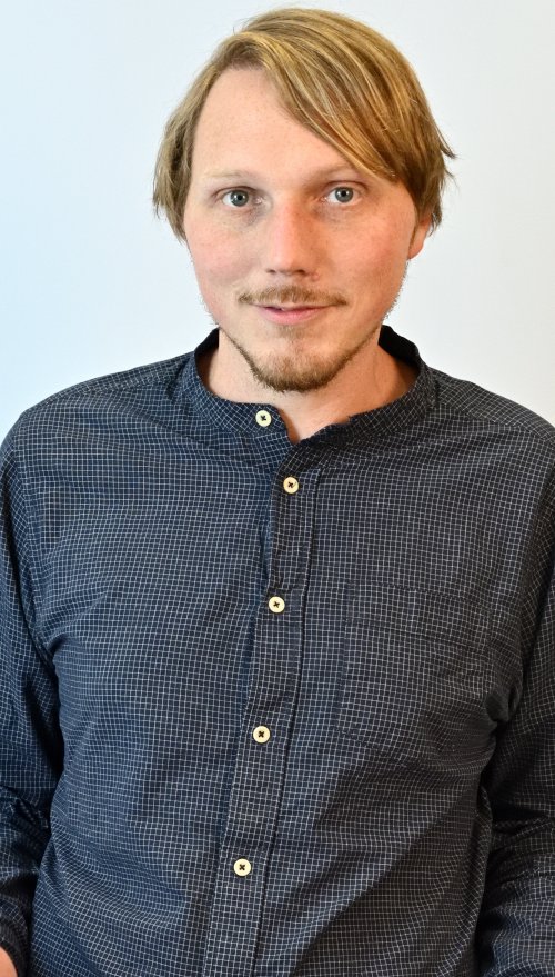 Ein Portraitfoto von Sören Barge, der weiße Haut und helle Haare hat und ein blaues Hemd trägt