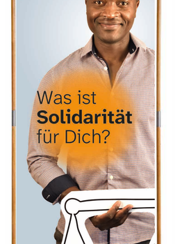 Ein großer Aufsteller, auf dem ein Mann mit schwarzer Hautfarbe und eine Hemd eine Waage in der Hand hält. Auf dem Banner steht: Was ist Solidarität für dich?