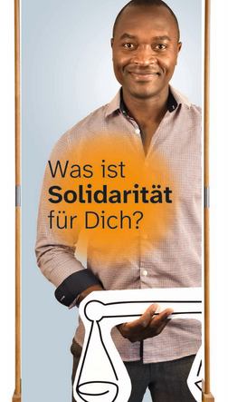 Ein großer Aufsteller, auf dem ein Mann mit schwarzer Hautfarbe und eine Hemd eine Waage in der Hand hält. Auf dem Banner steht: Was ist Solidarität für dich?