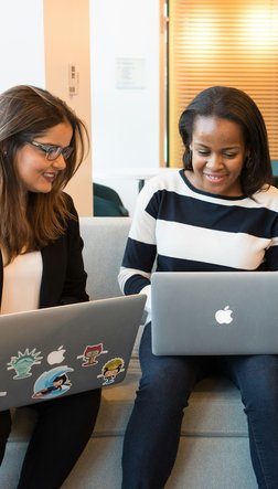 Drei Frauen sitzen und gucken zusammen auf ihren Komputern und reden