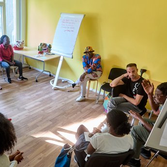 Menschen stehen im Kreis und haben zwischen sich ein Netz aus einem Faden gespannt