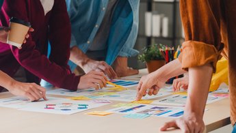 Hände stützen sich auf einen Tisch voll mit Notizen, Papieren und Post-its
