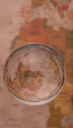 Eine Glaskugel schwebt vor einer Weltkarte, in ihr sieht man die Karte gespiegelt und auf den Kopf gestellt