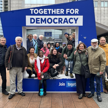 Eine Gruppe Menschen steht vor dem EU Parlament vor einem großen Schild, auf dem "Together for Democracy" steht